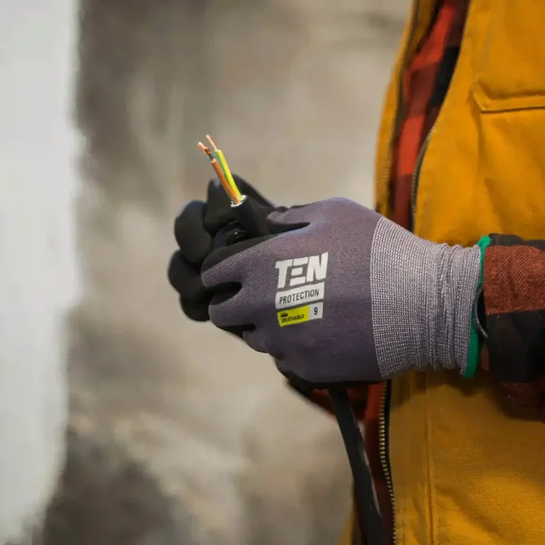 Mise en sécurité - Leon Services Main dans un gant, tenant des fils électriques colorés. Vêtements de travail visibles d'un électricien à Paris.